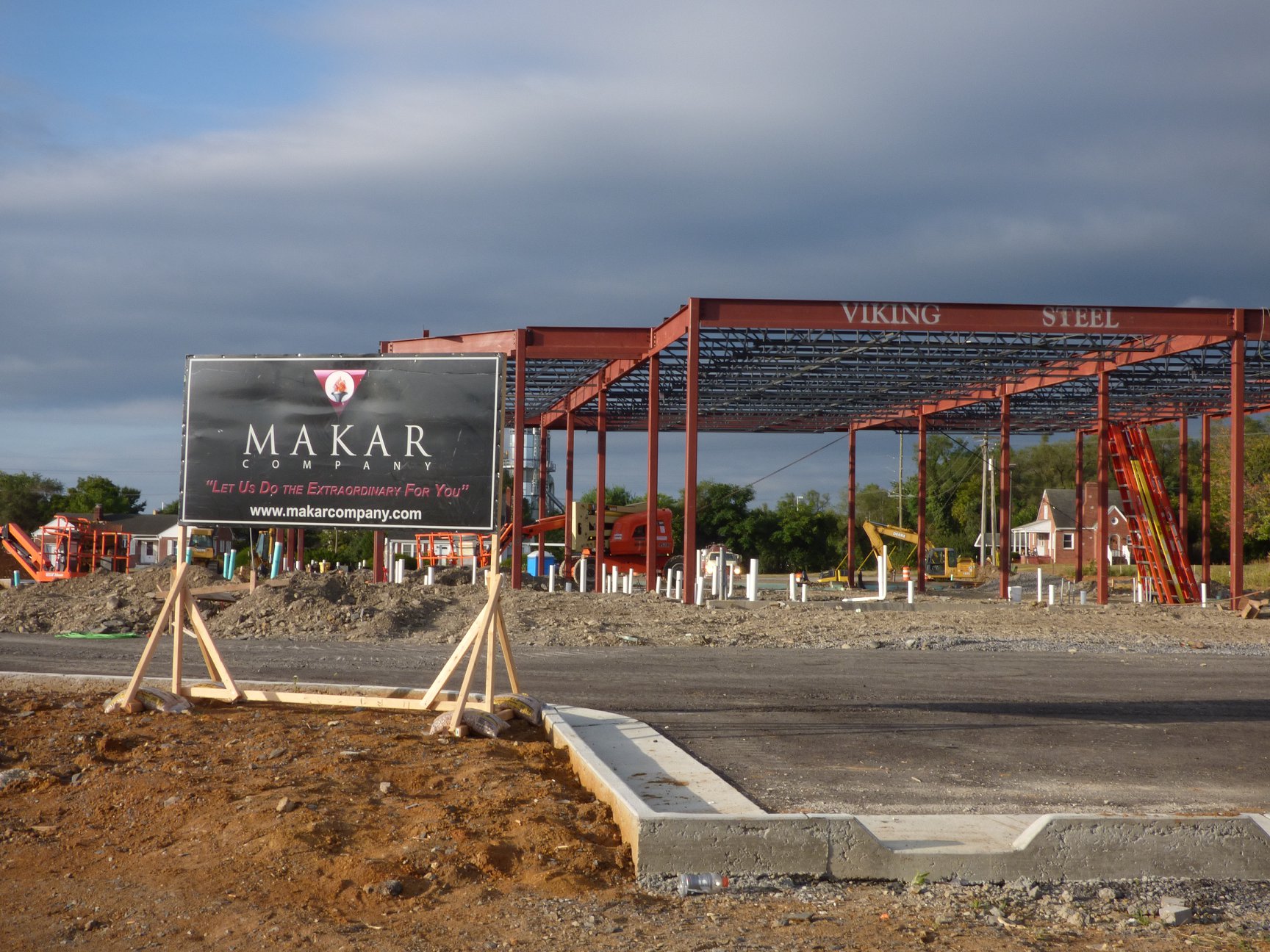 Construction site with a steel frame structure labeled "Viking Steel." A sign for "Makar Company" stands in the foreground. Cloudy sky hints at upcoming weather.